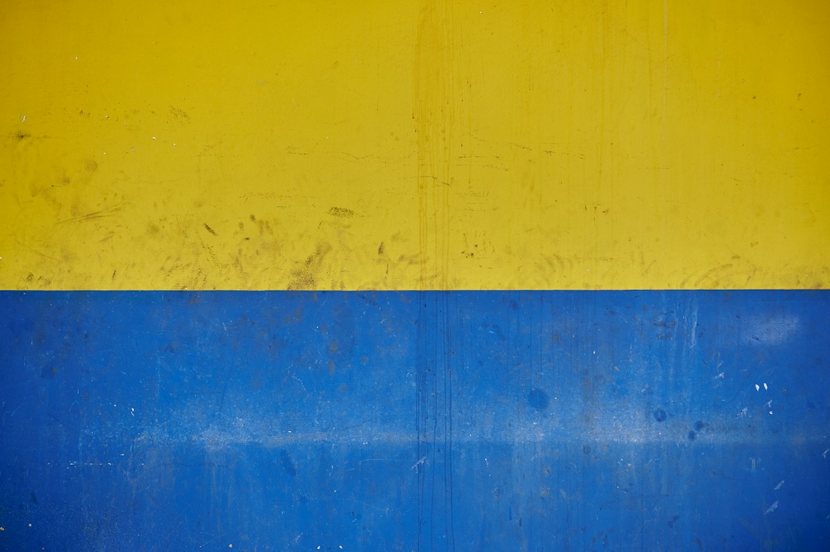 A weathered wall painted yellow and blue, photographed in Harare