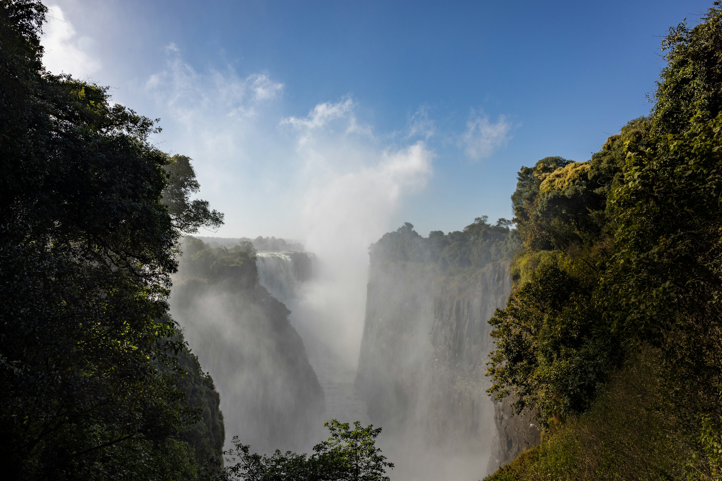 Victoria Falls spilling into a tree-lined gorge beneath a blue sky